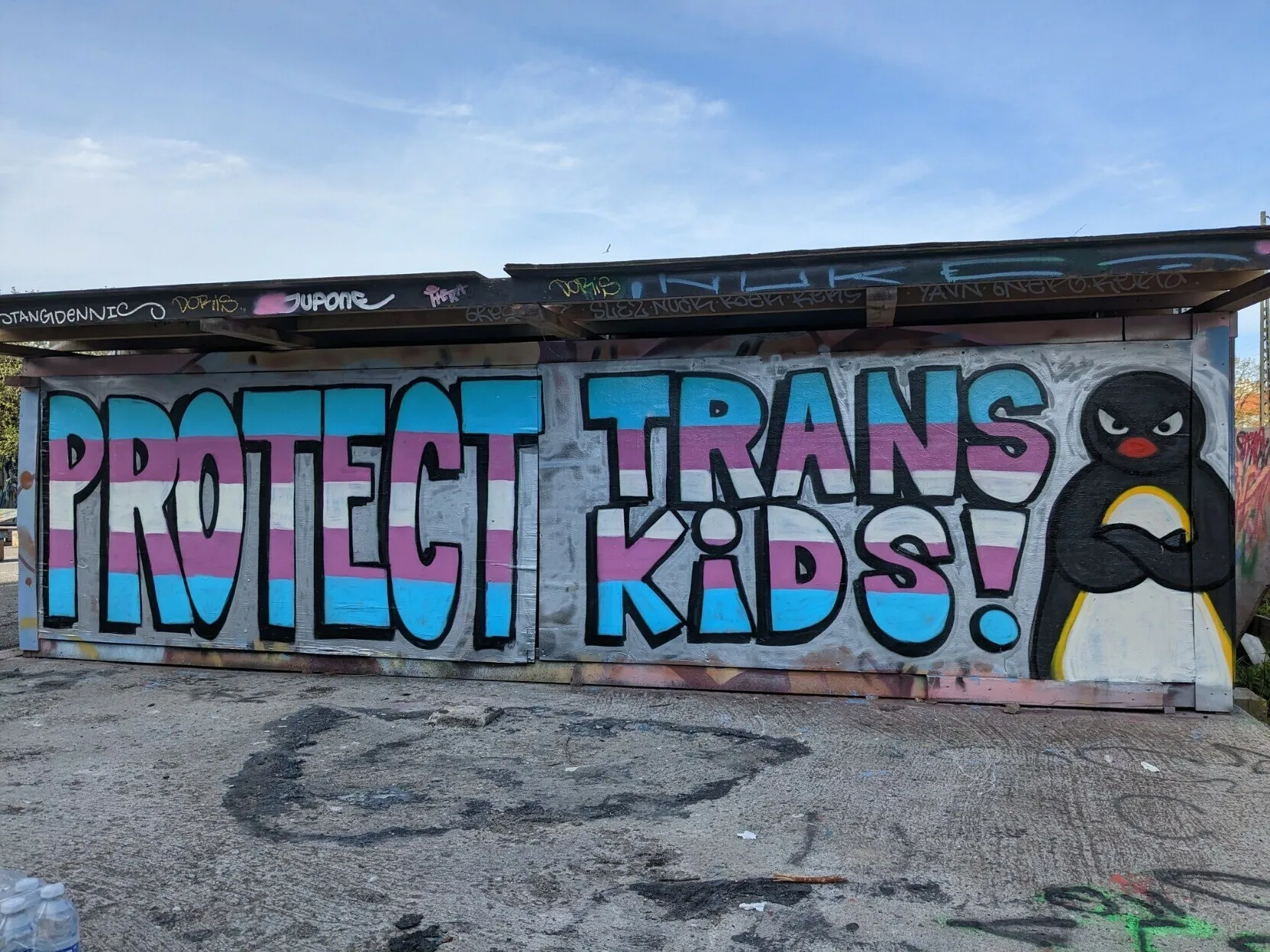 Tagged wall with the phrase "Protect Trans Kids!" With an unamused penguin on the right of the phrase.